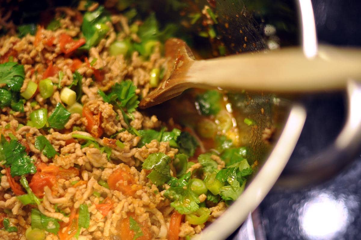 Nam prik ong khas Thailand dengan daging cincang, tomat, daun ketumbar, dan daun bawang dimasak dalam wajan dengan sendok kayu.