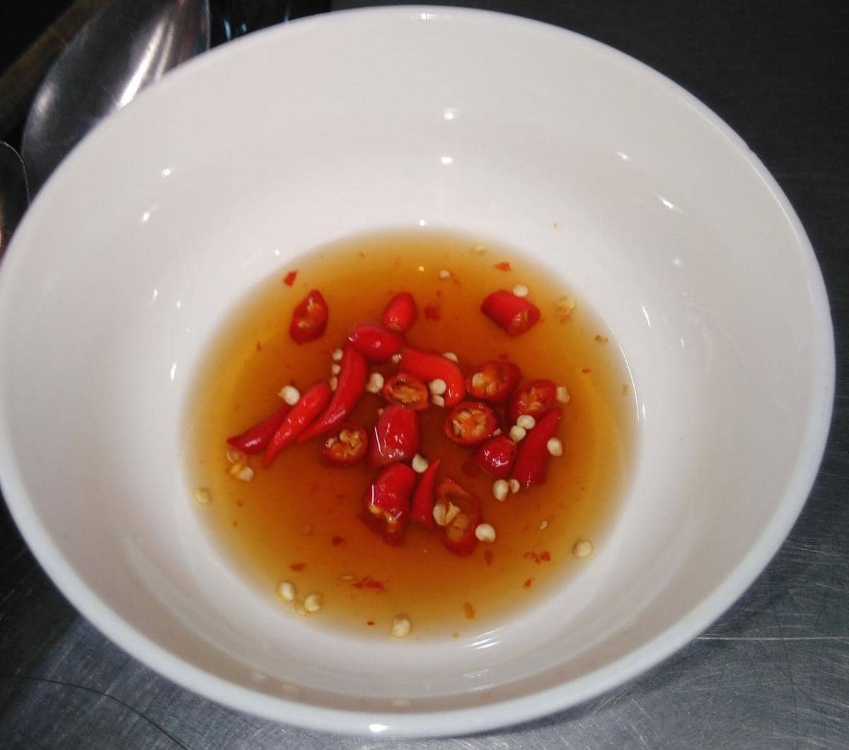 Semangkuk saus nuoc mam cham khas Vietnam berwarna cokelat keemasan dengan potongan cabai merah di dalamnya.