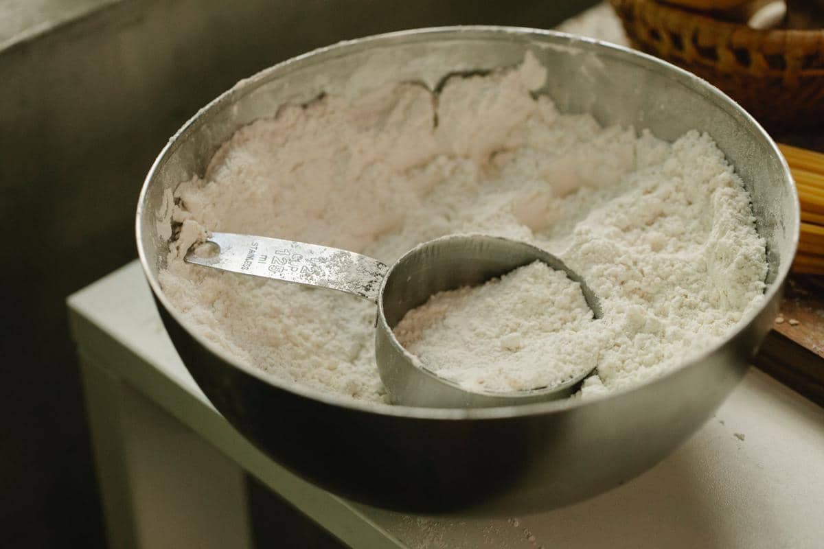 Tepung terigu protein tinggi dalam mangkuk logam dengan sendok takar stainless steel di atas meja dapur.