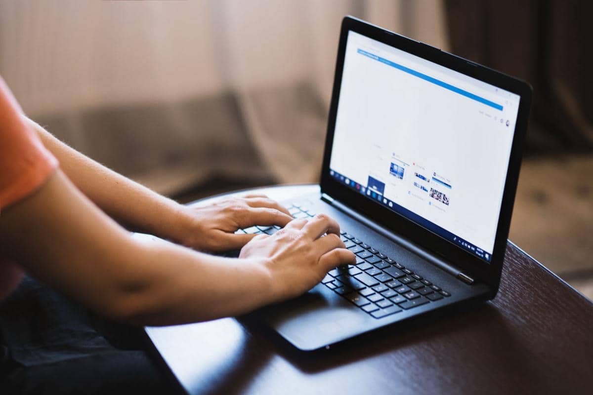 Seseorang mengetik di laptop sambil melakukan pencarian informasi di internet di atas meja kayu dalam ruangan.