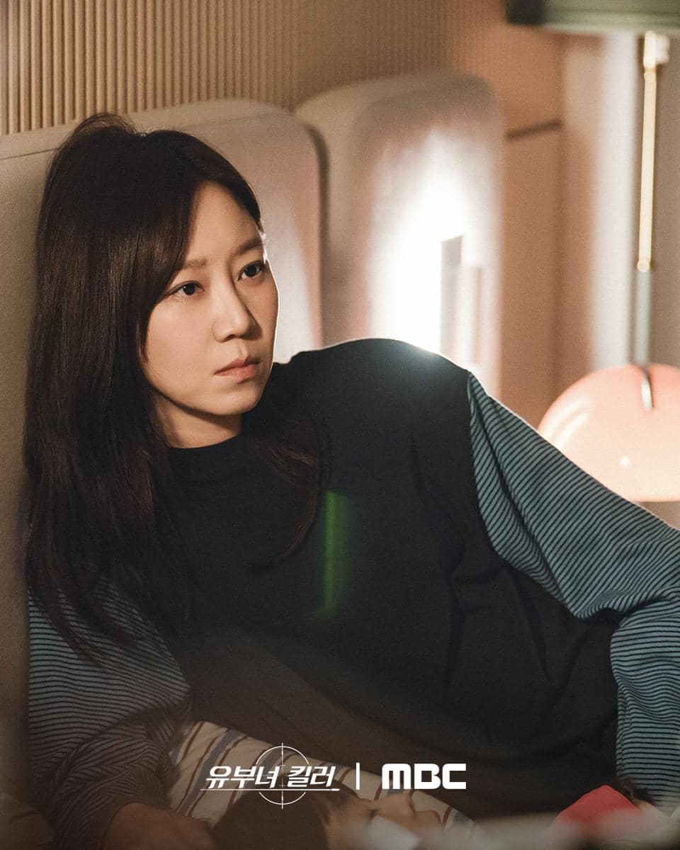 Seorang wanita berambut panjang mengenakan sweater gelap sedang berbaring di sofa dengan ekspresi serius dalam adegan Killer of Married Woman.