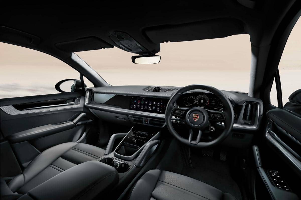 Interior Porsche Cayenne dengan desain modern, layar sentuh lebar di dashboard, dan setir berlogo Porsche di sisi kanan.
