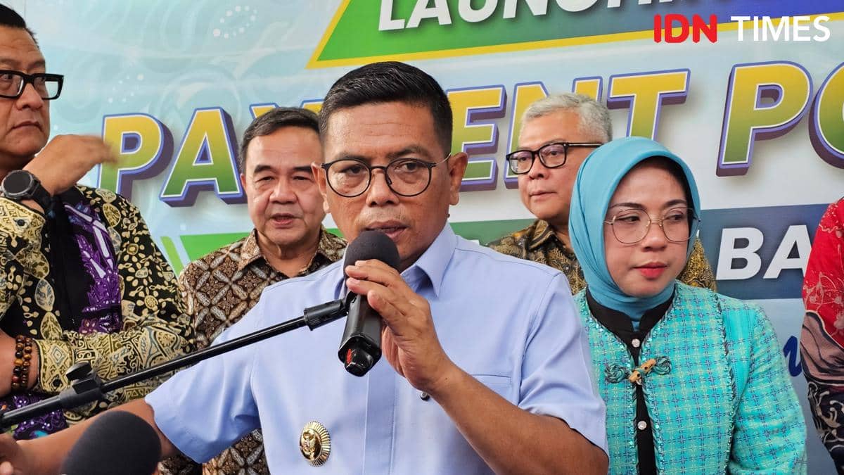 Seorang pria berbaju biru berbicara di depan mikrofon dengan beberapa orang berdiri di belakangnya dalam sebuah acara peluncuran.
