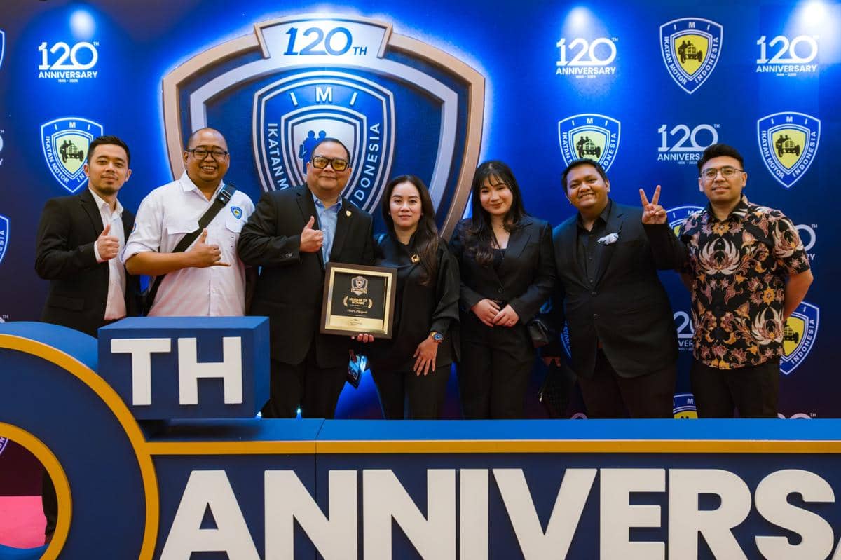 Sekelompok orang berpose bersama di acara IMI Awards 2026, salah satu di antaranya memegang plakat penghargaan di depan latar logo Ikatan Motor Indonesia.