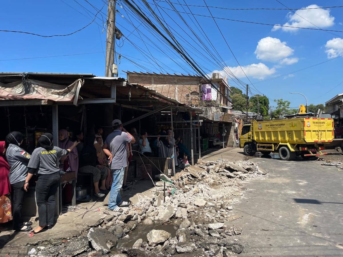 Petugas Satpol PP dan warga berada di lokasi pembongkaran pasar tumpah di Jalan AMD, Kecamatan Manggala, Makassar, dengan truk kuning pengangkut sampah di dekatnya.