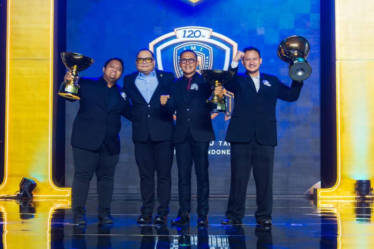 Empat pria berpakaian jas hitam berpose di panggung sambil memegang piala besar pada ajang IMI Awards 2026.