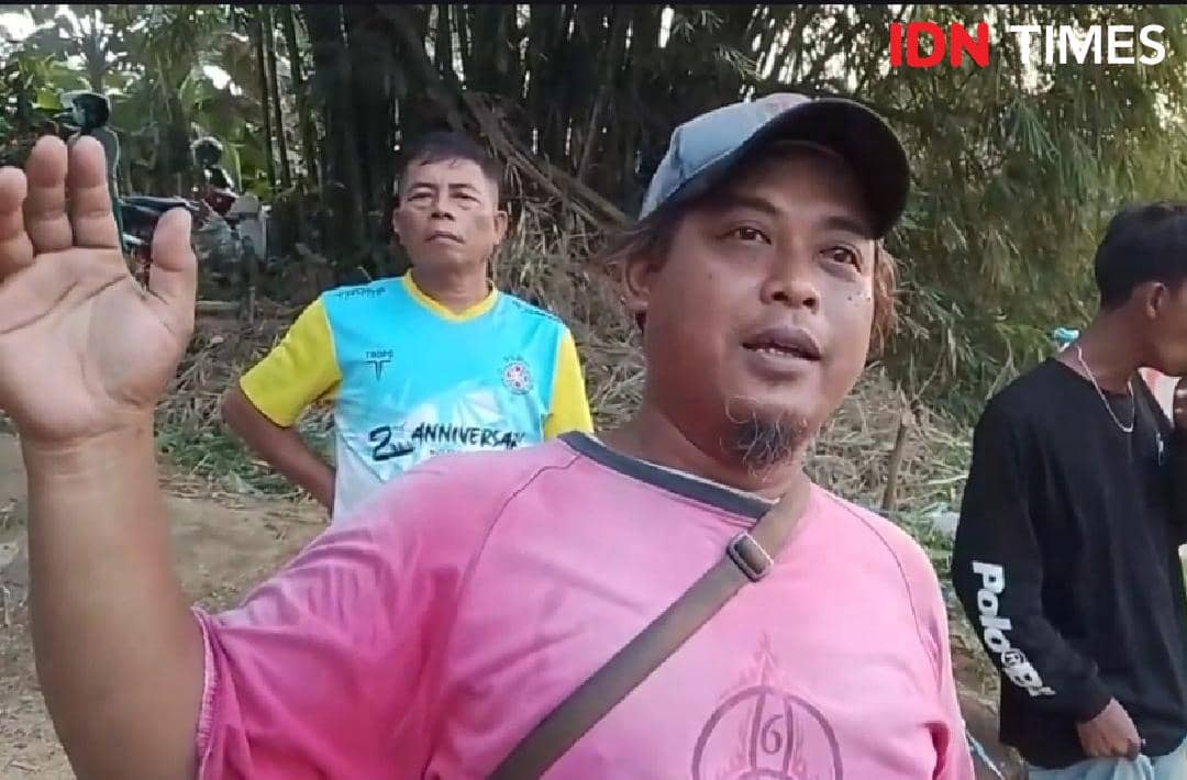 Seorang operator perahu pasir mengenakan kaus merah muda berbicara di area tepian sungai dengan beberapa orang di sekitarnya.
