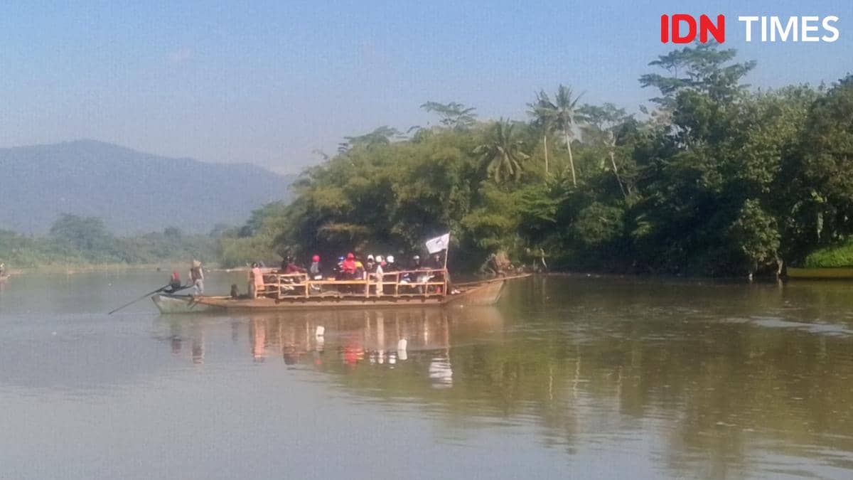 Sejumlah warga menaiki perahu penyeberangan di Sungai Serayu dengan latar pepohonan hijau dan pegunungan di kejauhan.