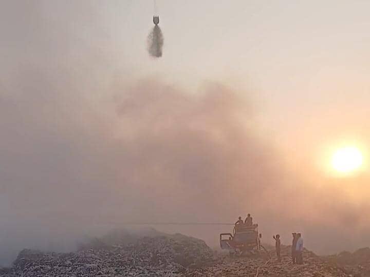 Helikopter melakukan water bombing untuk memadamkan kebakaran di TPA Jatiwaringin saat matahari terbenam dengan asap tebal di udara.