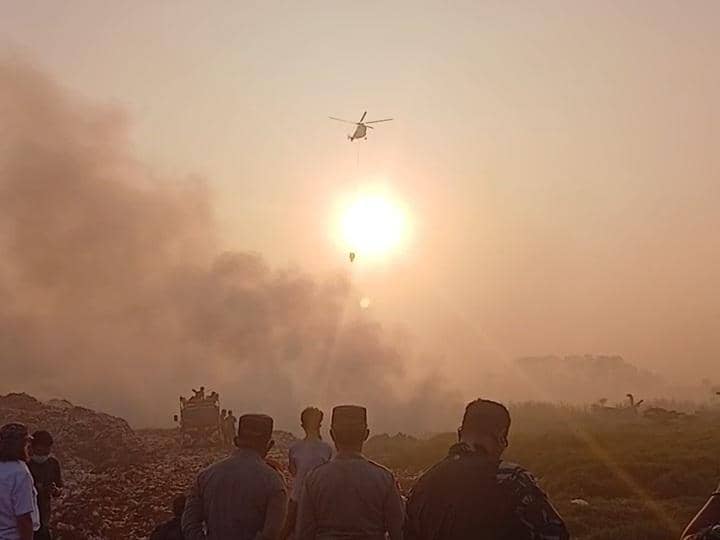 Helikopter BNPB melakukan water bombing untuk memadamkan kebakaran di TPA Jatiwaringin saat matahari terbenam dengan asap tebal di udara.