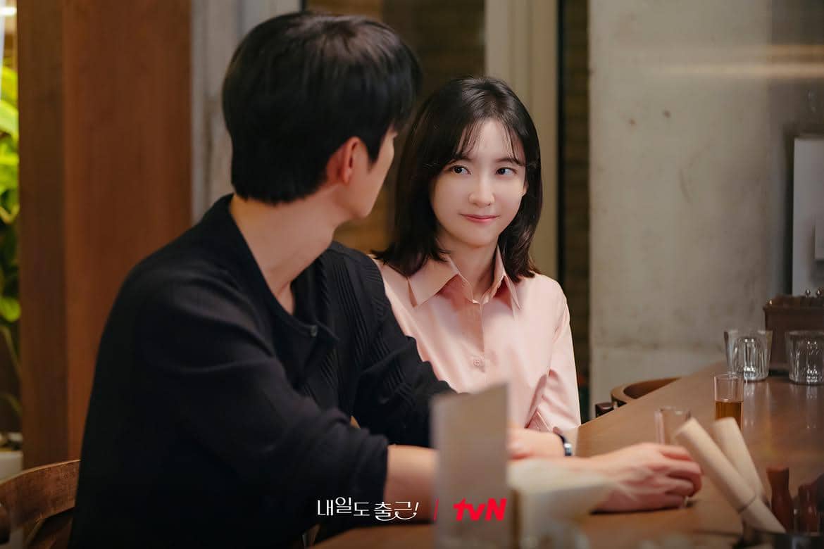 Dua orang duduk di meja bar, saling menatap dengan ekspresi hangat dalam adegan drama See You at Work Tomorrow!.