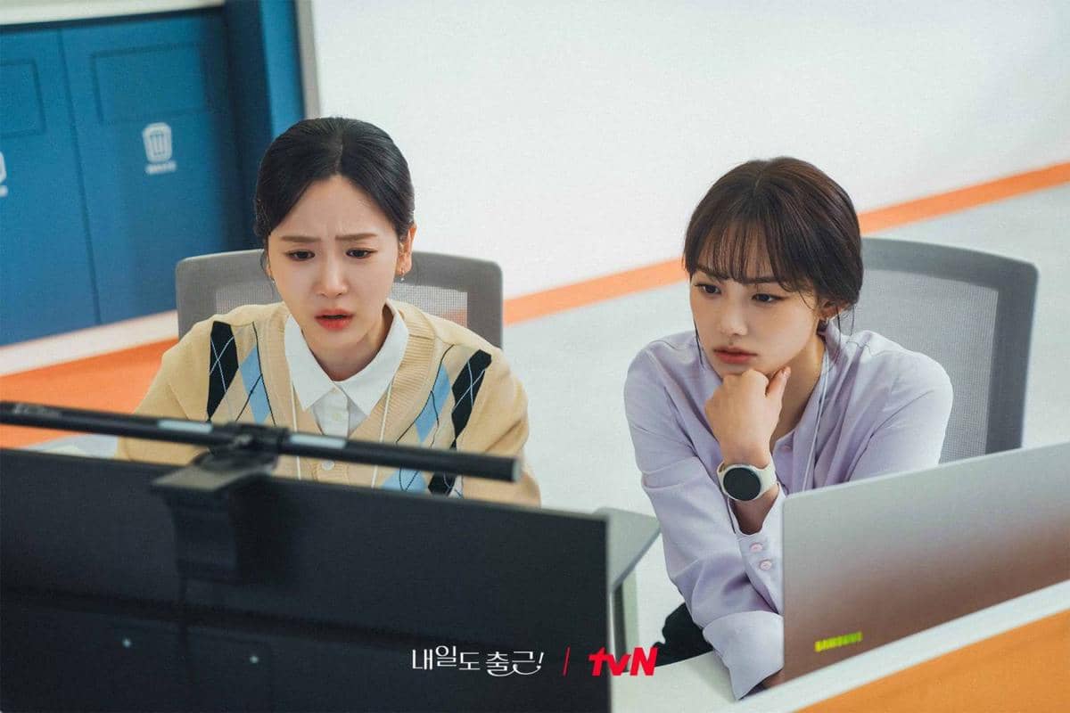 Dua wanita sedang duduk di depan komputer di kantor, tampak serius memperhatikan layar dalam cuplikan drama Korea See You at Work Tomorrow.
