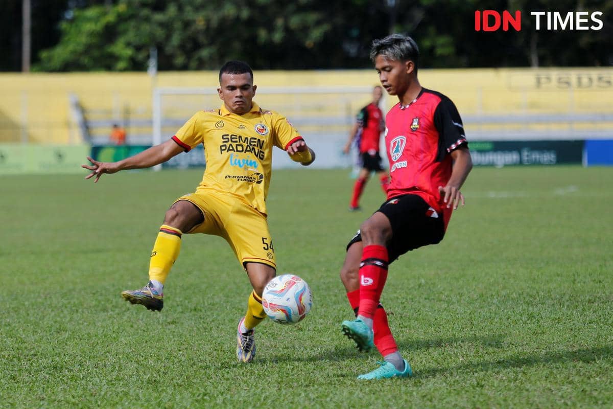 Pemain Semen Padang mengenakan seragam kuning berduel memperebutkan bola dengan pemain lawan berseragam merah di lapangan hijau.