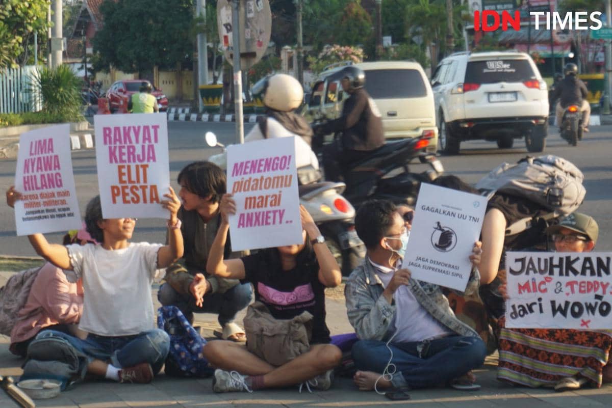 Sejumlah peserta aksi Suara Ibu Indonesia duduk di trotoar sekitar Bundaran UGM Sleman sambil memegang poster protes bertuliskan berbagai pesan sosial dan politik.