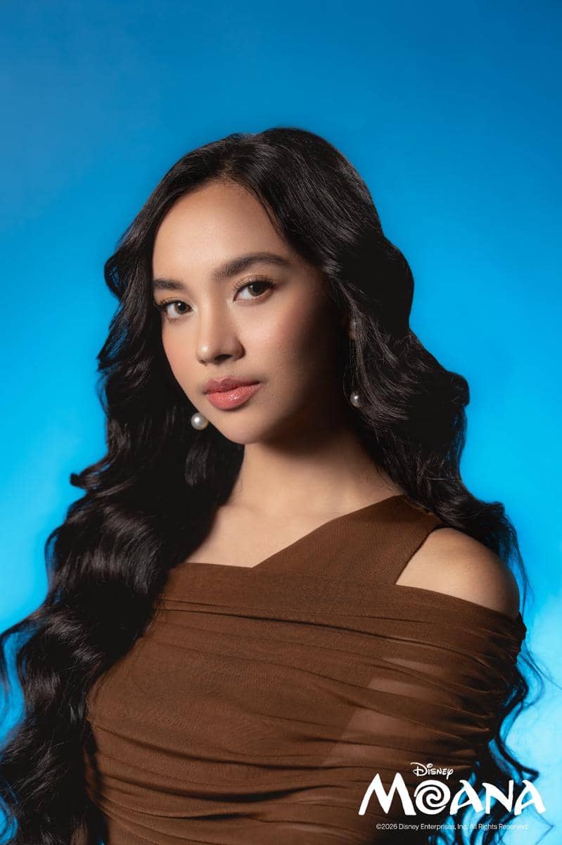 Seorang perempuan berambut panjang bergelombang mengenakan gaun cokelat berpose di latar biru dengan logo Disney Moana di sudut gambar.