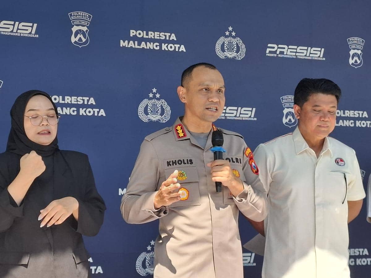 Seorang perwira polisi berbicara di depan mikrofon didampingi dua orang, dengan latar belakang bertuliskan Polresta Malang Kota.