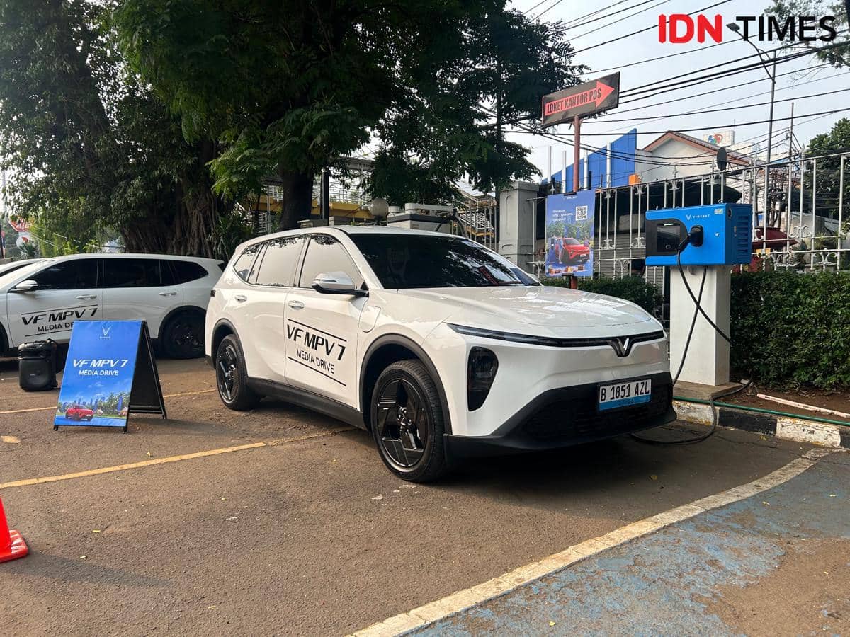 Mobil listrik VinFast VF MPV 7 berwarna putih sedang mengisi daya di stasiun pengisian kendaraan listrik di area parkir.