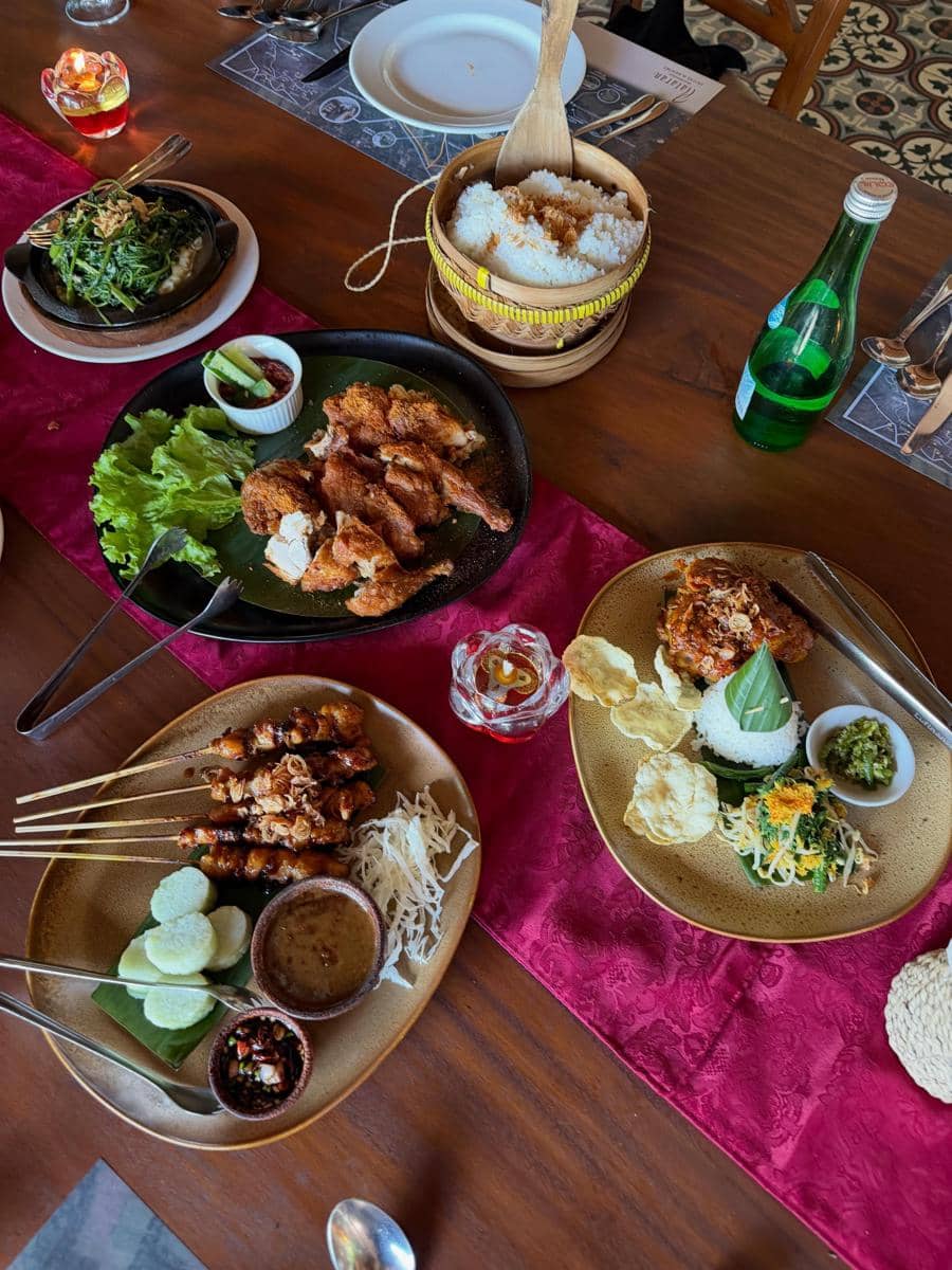 Hidangan khas Indonesia tersaji di atas meja kayu dengan nasi, ayam goreng, sate, sayur, dan sambal di restoran di Yogyakarta.