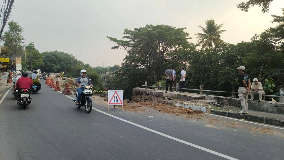 Beberapa pengendara motor melintas di Jalan Kebon Pedes Bogor dengan pengalihan lalu lintas akibat bekas longsor di tepi jalan.