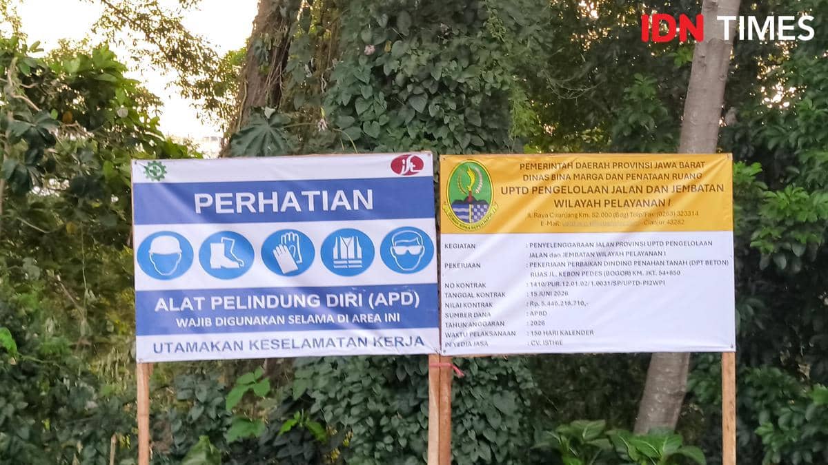 Papan informasi proyek perbaikan dinding penahan tanah di Kebon Pedes, Bogor, dengan petunjuk penggunaan alat pelindung diri bagi pekerja.