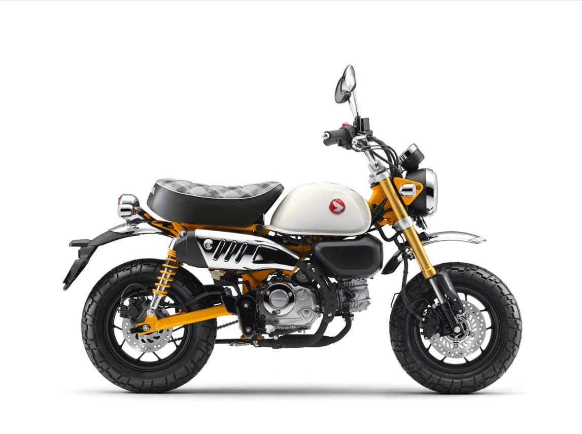 Motor mini Honda Monkey dengan kombinasi warna kuning dan putih, menampilkan desain retro dengan jok hitam bermotif dan detail krom.