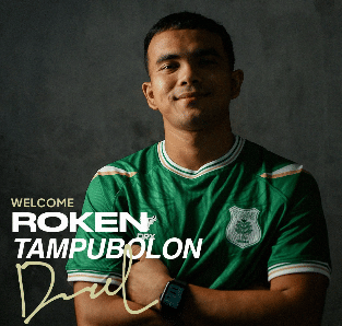 Seorang pria mengenakan jersey hijau PSMS Medan berdiri dengan tangan terlipat di depan latar gelap, tampak percaya diri.