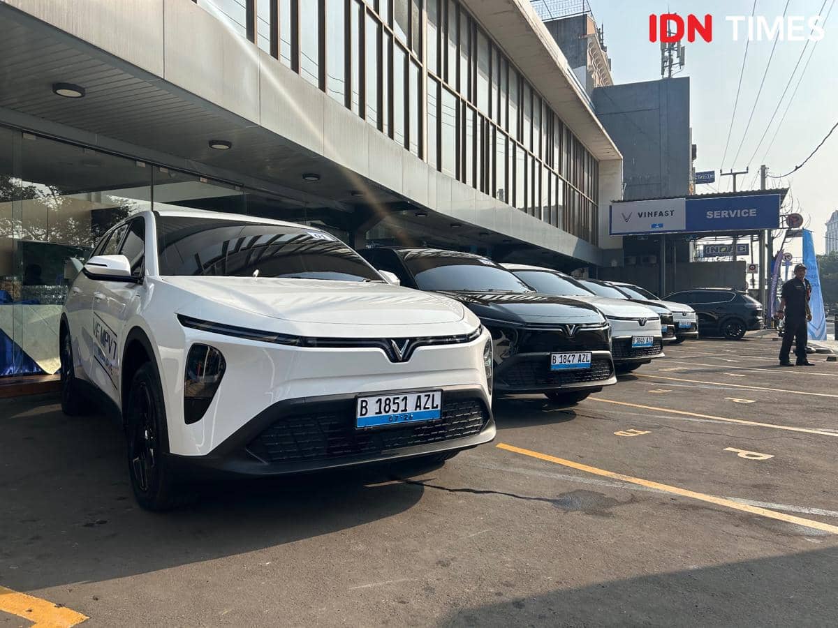 Deretan mobil VinFast VF MPV 7 berwarna putih dan hitam terparkir di depan gedung layanan VinFast dengan area parkir yang rapi.