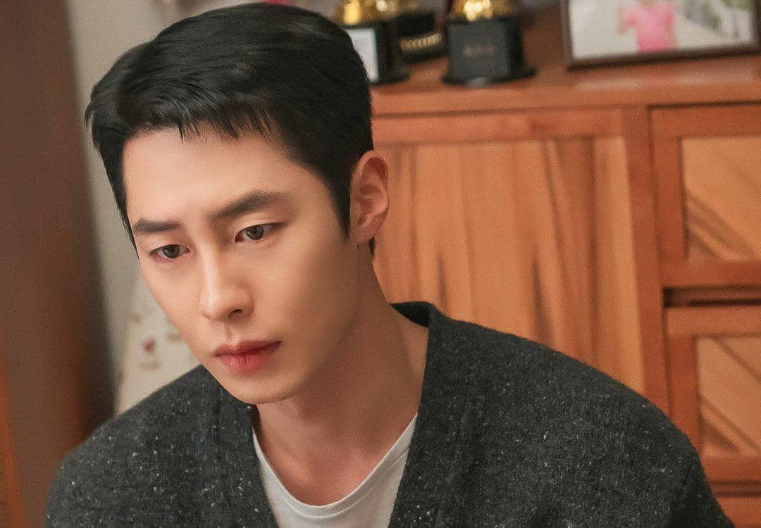 Seorang pria berambut pendek mengenakan kardigan abu-abu tampak serius dalam adegan drama Korea Doctor On The Edge.