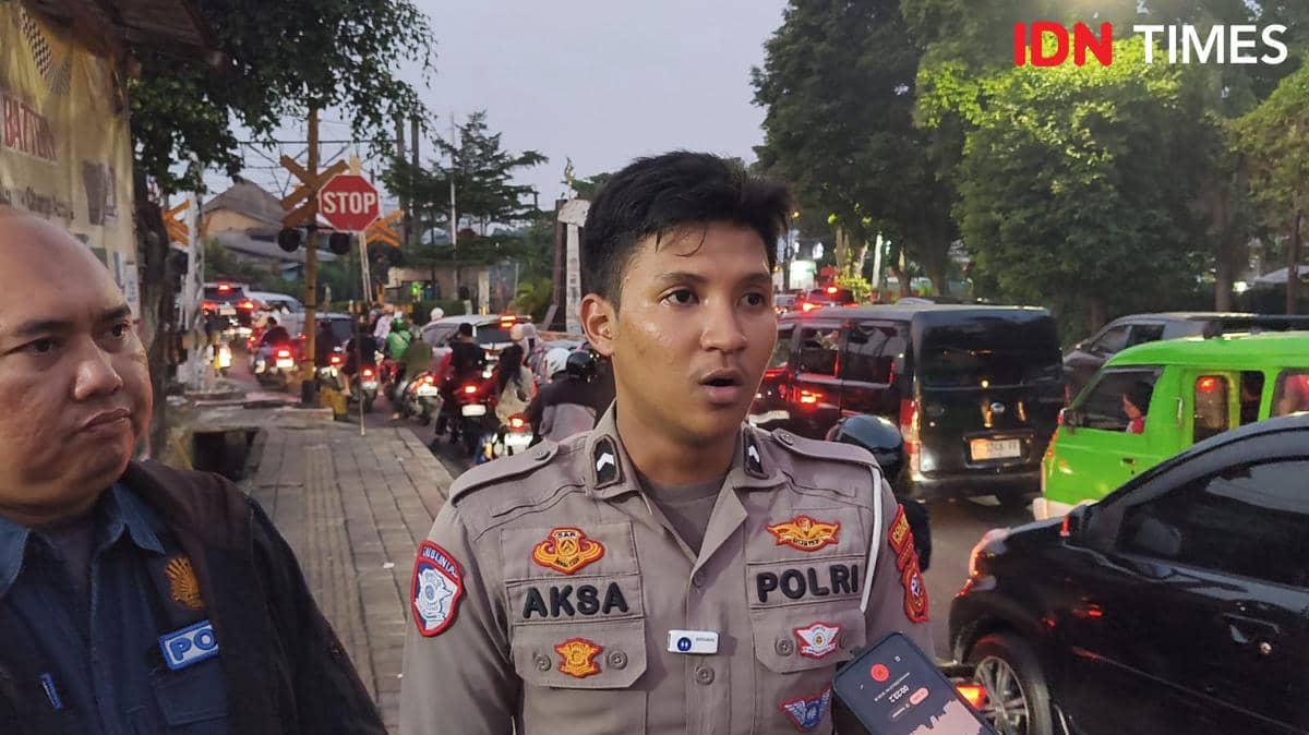 Seorang polisi lalu lintas berseragam memberikan penjelasan kepada wartawan di tepi jalan yang dipadati kendaraan pada sore hari.