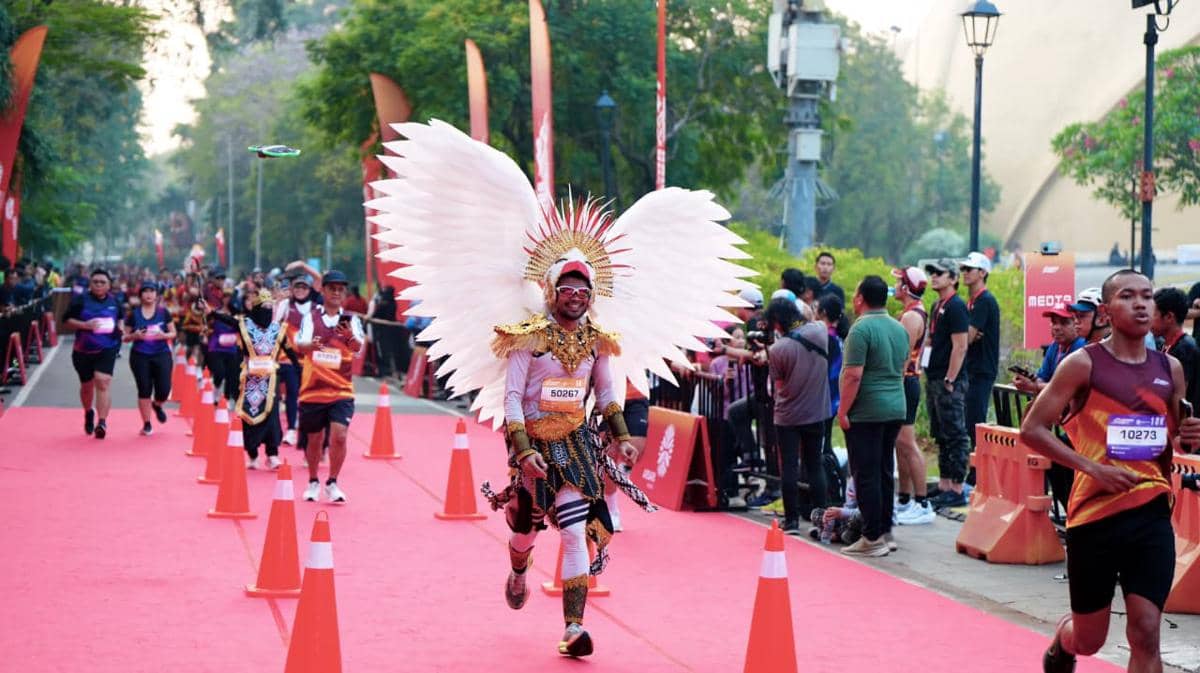 Peserta Bhinneka Run 2026 di Jakarta berlari mengenakan kostum unik dengan sayap besar putih di jalur lomba berkarpet merah.