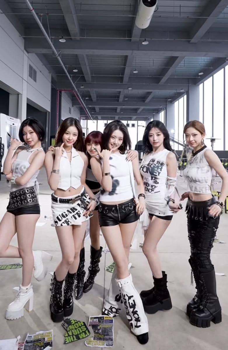 Enam anggota grup BABYMONSTER berpose bersama mengenakan busana bernuansa hitam putih di dalam ruangan industrial modern.
