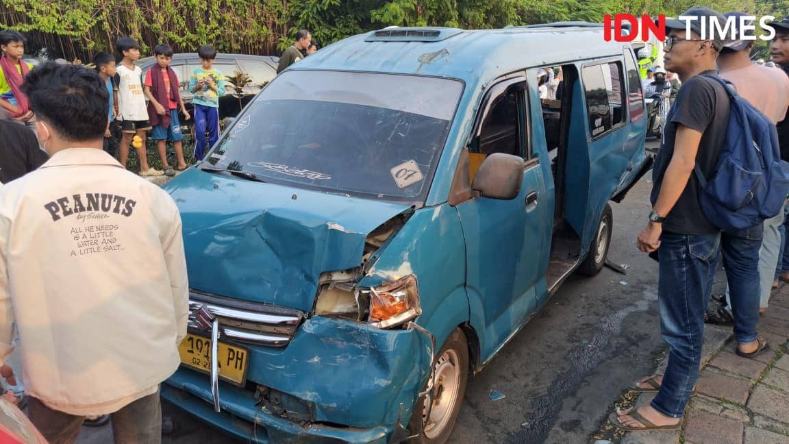 Angkot berwarna biru mengalami kerusakan parah di bagian depan setelah tabrakan beruntun, disaksikan warga di pinggir jalan.