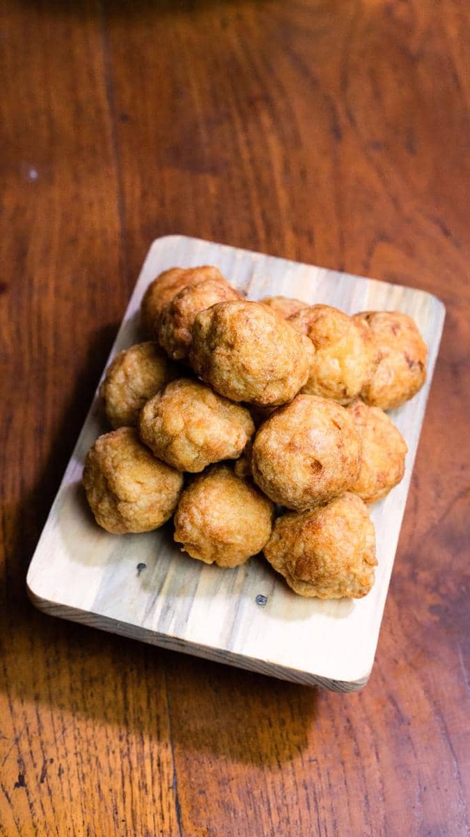 Beberapa perkedel kentang goreng berwarna keemasan tersusun di atas talenan kayu di meja makan berwarna cokelat.