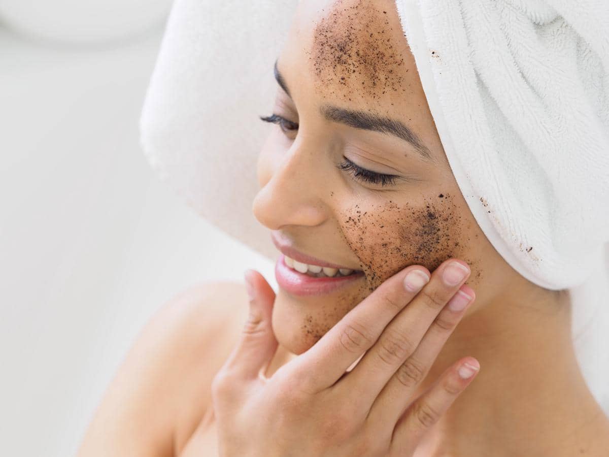 Perempuan tersenyum mengaplikasikan scrub wajah.