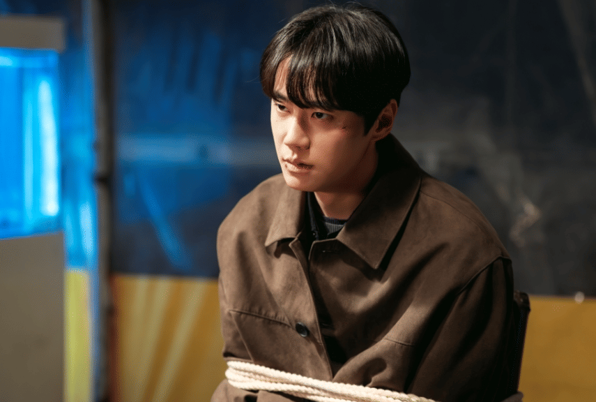 Seorang pria muda dengan jaket cokelat duduk terikat di kursi dalam adegan tegang dari drama Korea Reborn Rookie.