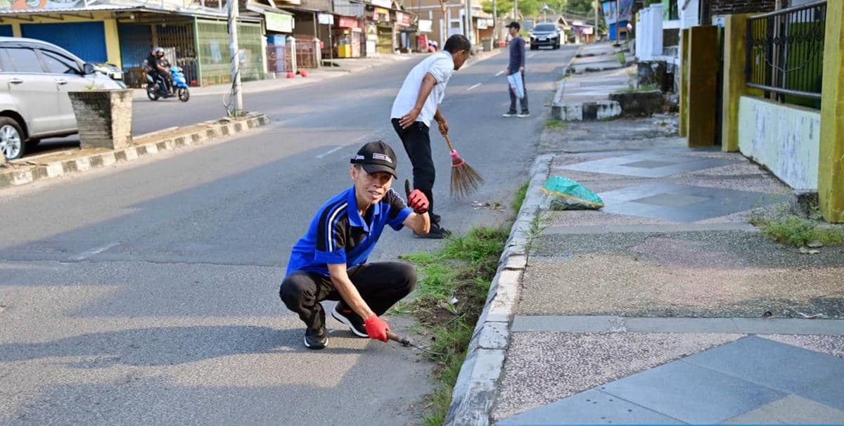 Beberapa aparatur sipil negara membersihkan rumput dan menyapu di tepi jalan protokol Kota Kalianda, Lampung Selatan.