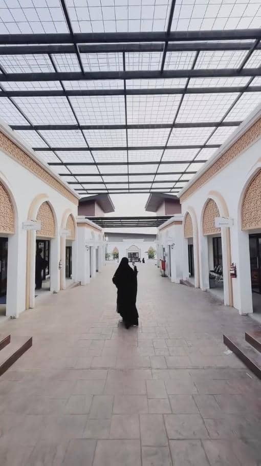 Seorang perempuan berpakaian hitam berjalan di lorong pesantren dengan arsitektur bergaya Timur Tengah dan atap kaca besar.