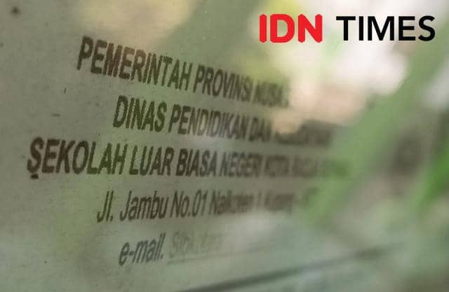 Tulisan alamat Sekolah Luar Biasa Negeri Kota Radja di Kota Kupang pada papan informasi dengan latar belakang buram.