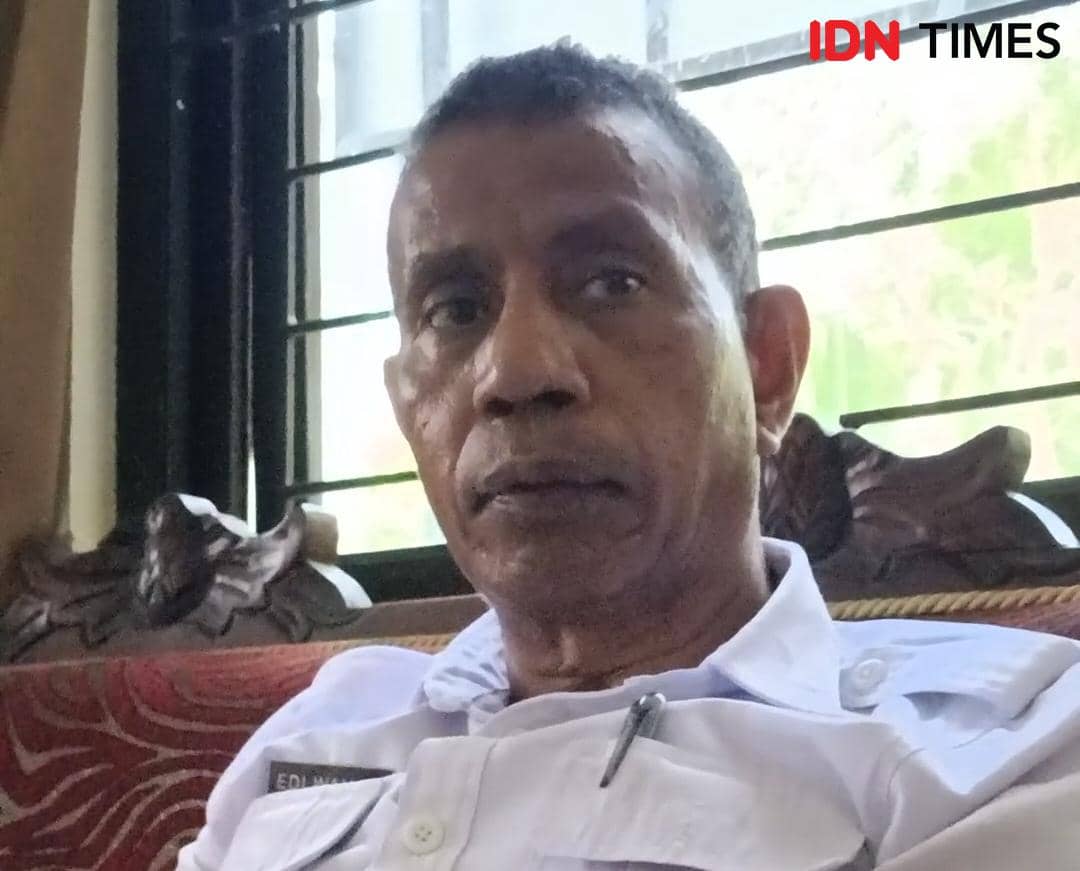 Seorang pria mengenakan seragam putih duduk di sofa dengan latar jendela berpagar besi di dalam ruangan yang terang.