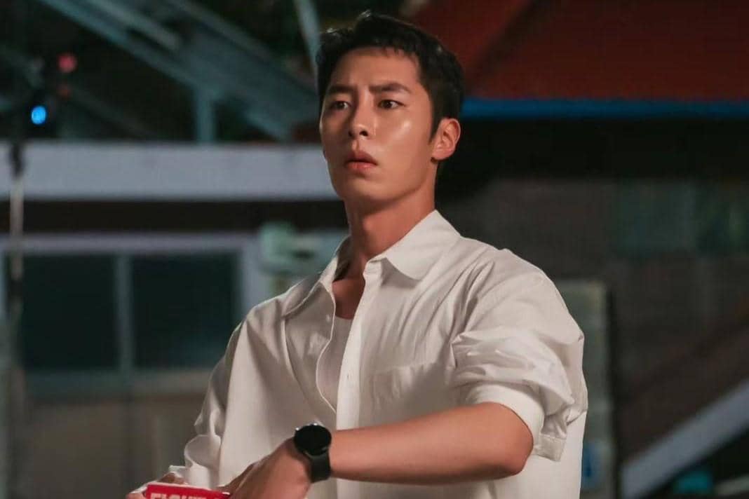 Seorang pria mengenakan kemeja putih dengan ekspresi serius dalam cuplikan drama Doctor On The Edge di malam hari.