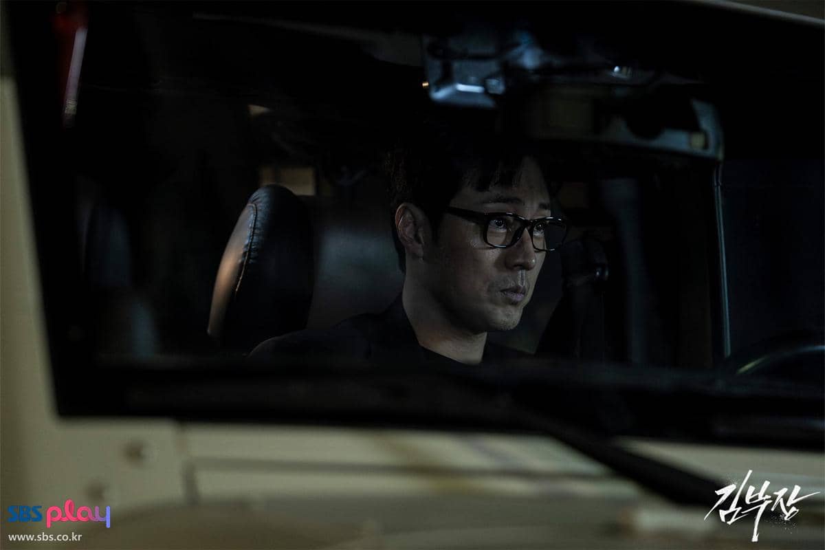 Seorang pria berkacamata duduk di dalam mobil pada malam hari dalam adegan drama Agent Kim Reactivated produksi SBS.