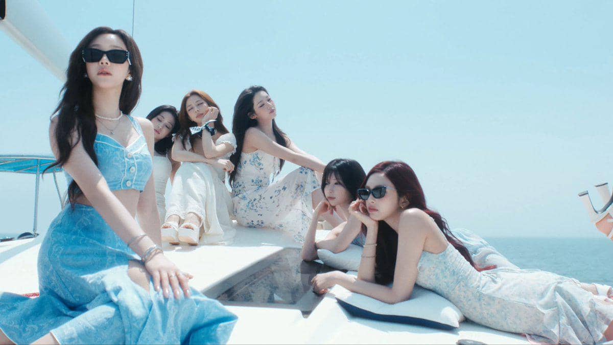 Para anggota BABYMONSTER mengenakan gaun musim panas berwarna pastel berpose santai di atas kapal di bawah langit cerah di laut.