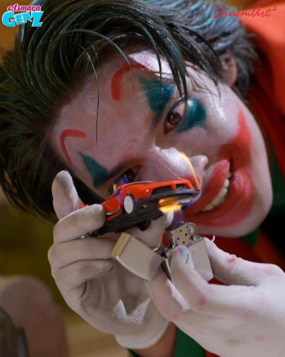 Seorang pria dengan riasan wajah bergaya Joker memegang mobil mainan merah dan pemantik api di adegan serial Asmara Gen Z.