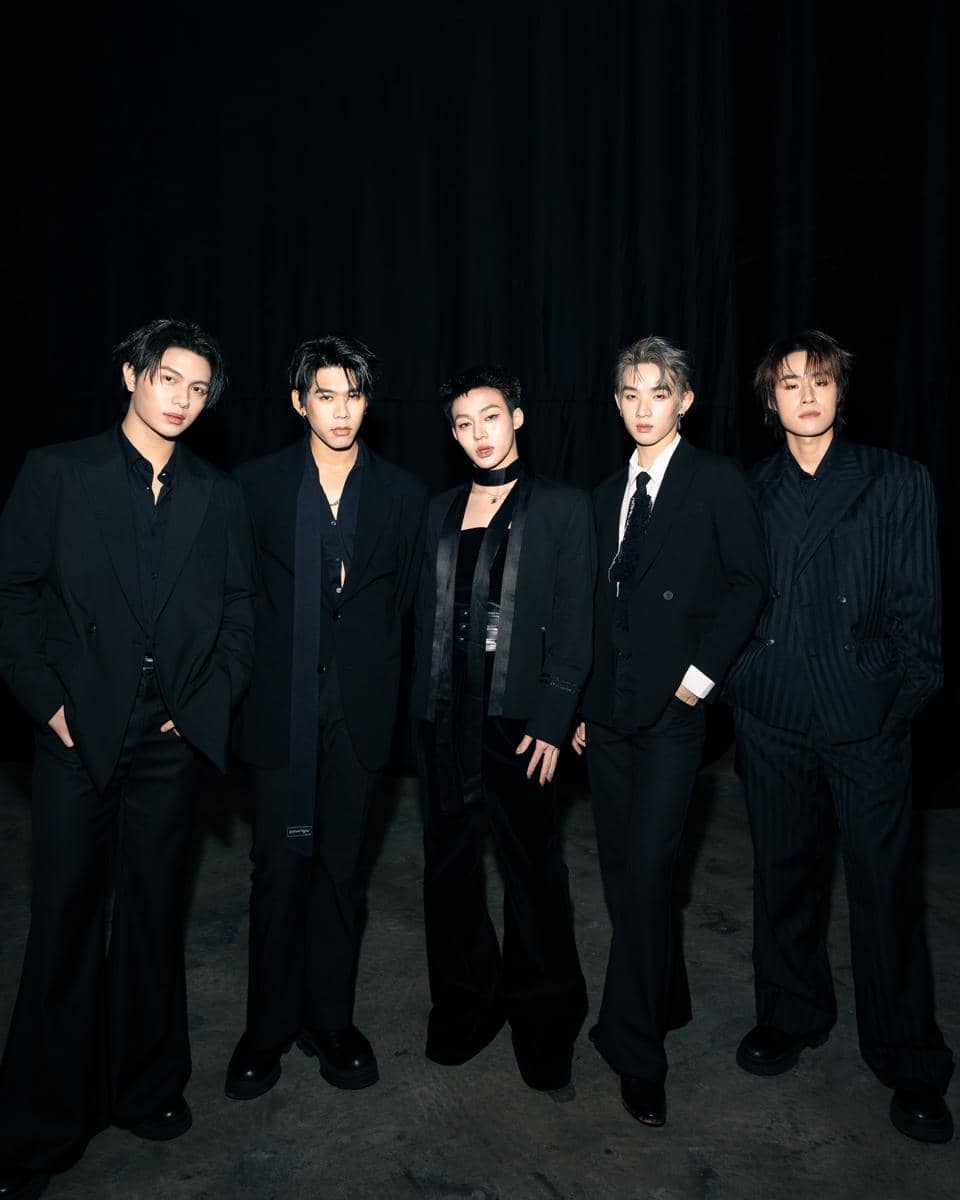 Lima anggota grup musik LYKN berdiri berjejer mengenakan setelan hitam elegan di depan latar belakang gelap.