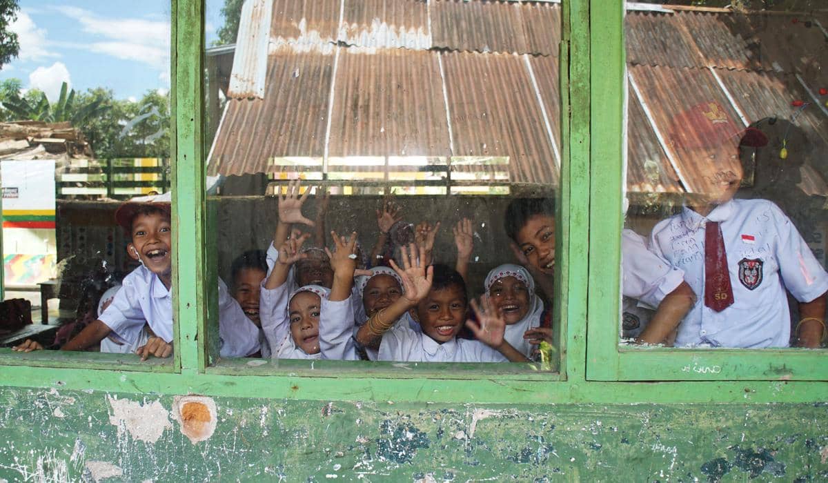 Anak-anak SD melambaikan tangan dari jendela sekolah di daerah pedesaan