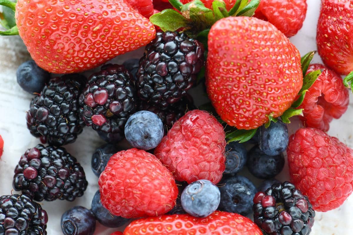 Campuran buah beri segar terdiri dari stroberi, raspberry, blueberry, dan blackberry dengan warna merah, ungu, dan biru cerah.