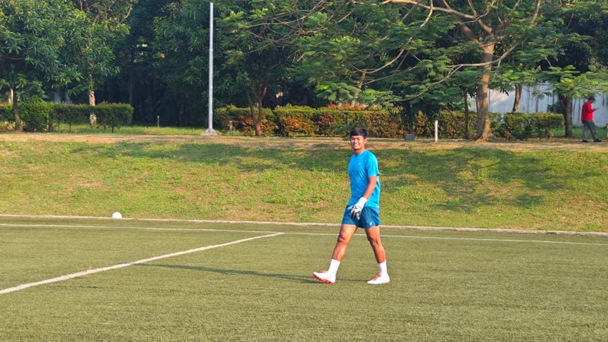Seorang peserta mengenakan pakaian olahraga biru dan sepatu putih berjalan di lapangan rumput saat kegiatan ASICS Summer Camp 2026.