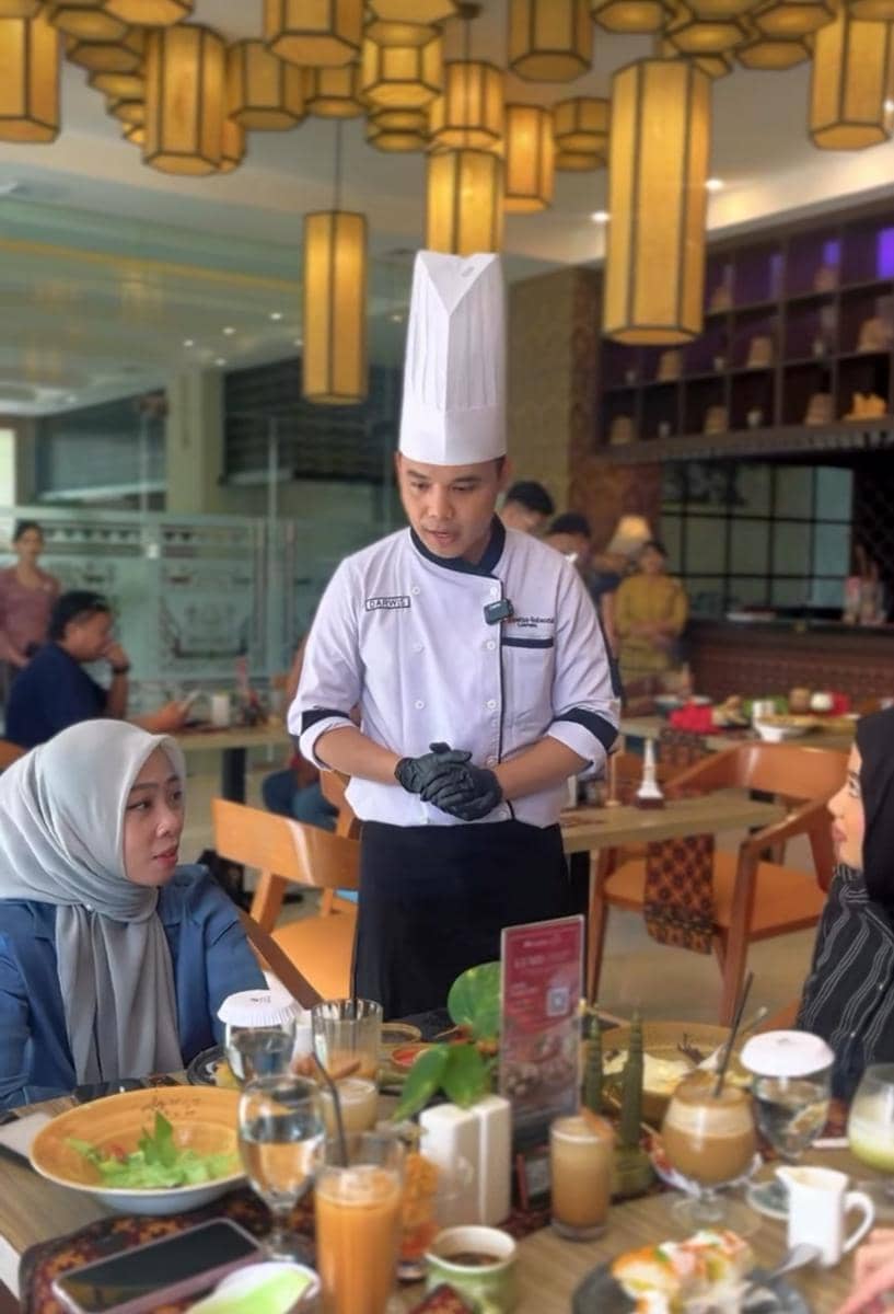 Seorang koki berbicara dengan dua tamu wanita di restoran Swiss-Belhotel Lampung dengan meja penuh hidangan dan minuman.