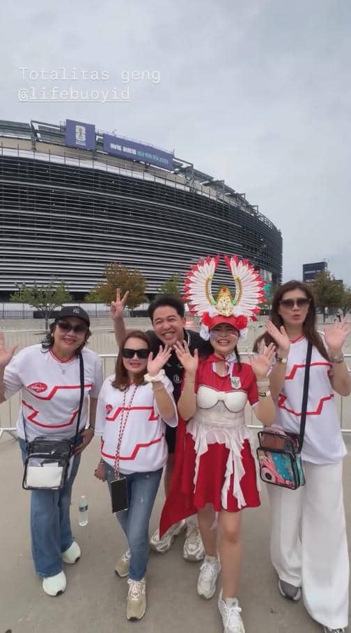 Sekelompok orang mengenakan kostum dan kaus bertema Indonesia berpose gembira di depan stadion besar saat Piala Dunia 2026.