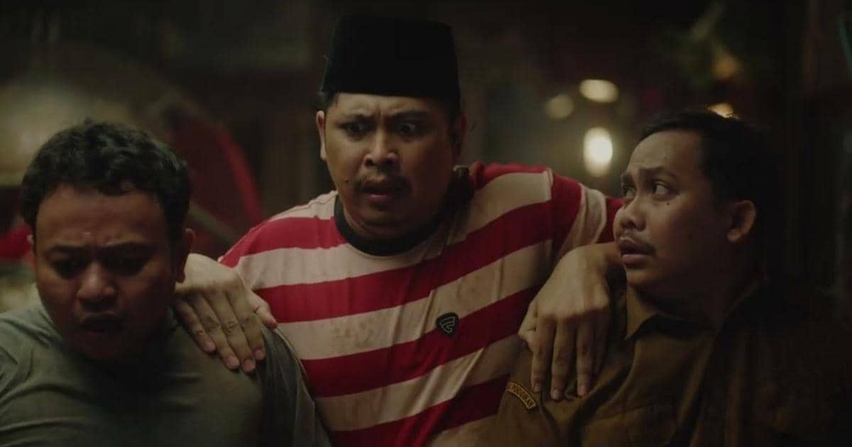 Tiga pria berdiri berdekatan dengan ekspresi tegang dalam adegan film Foufo, salah satunya mengenakan kaus bergaris merah putih dan peci hitam.